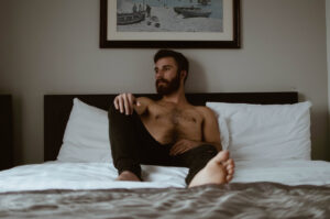 shirtless man in bedroom scene looking out window